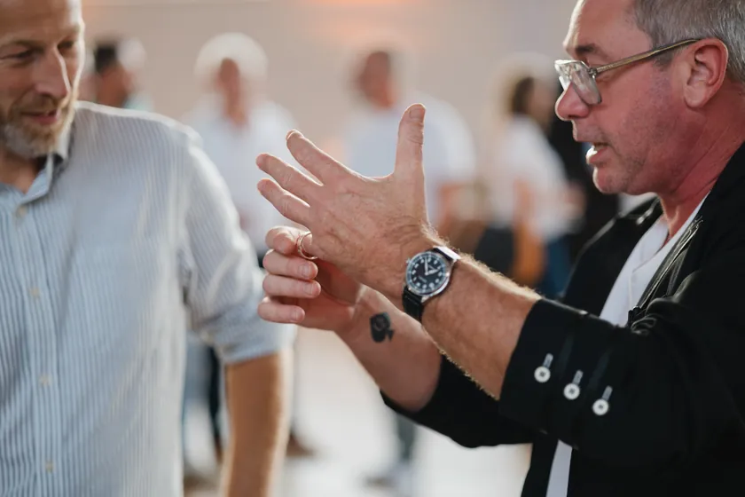 Vince montre une pièce au creux de sa main à un invité, pendant un cocktail